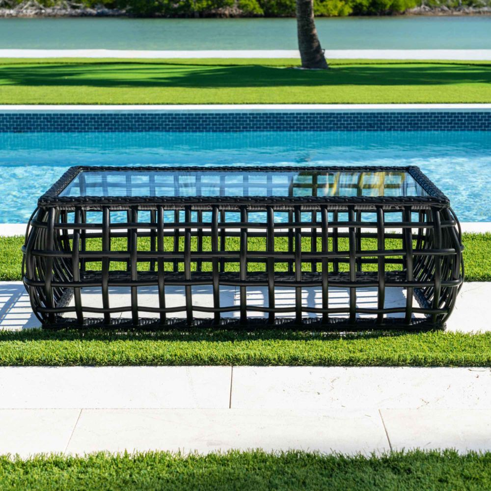 Black woven outdoor table by a poolside with green grass and water in the background
