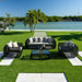 Outdoor patio set with black wicker furniture and white cushions on a grassy area by a waterfront.