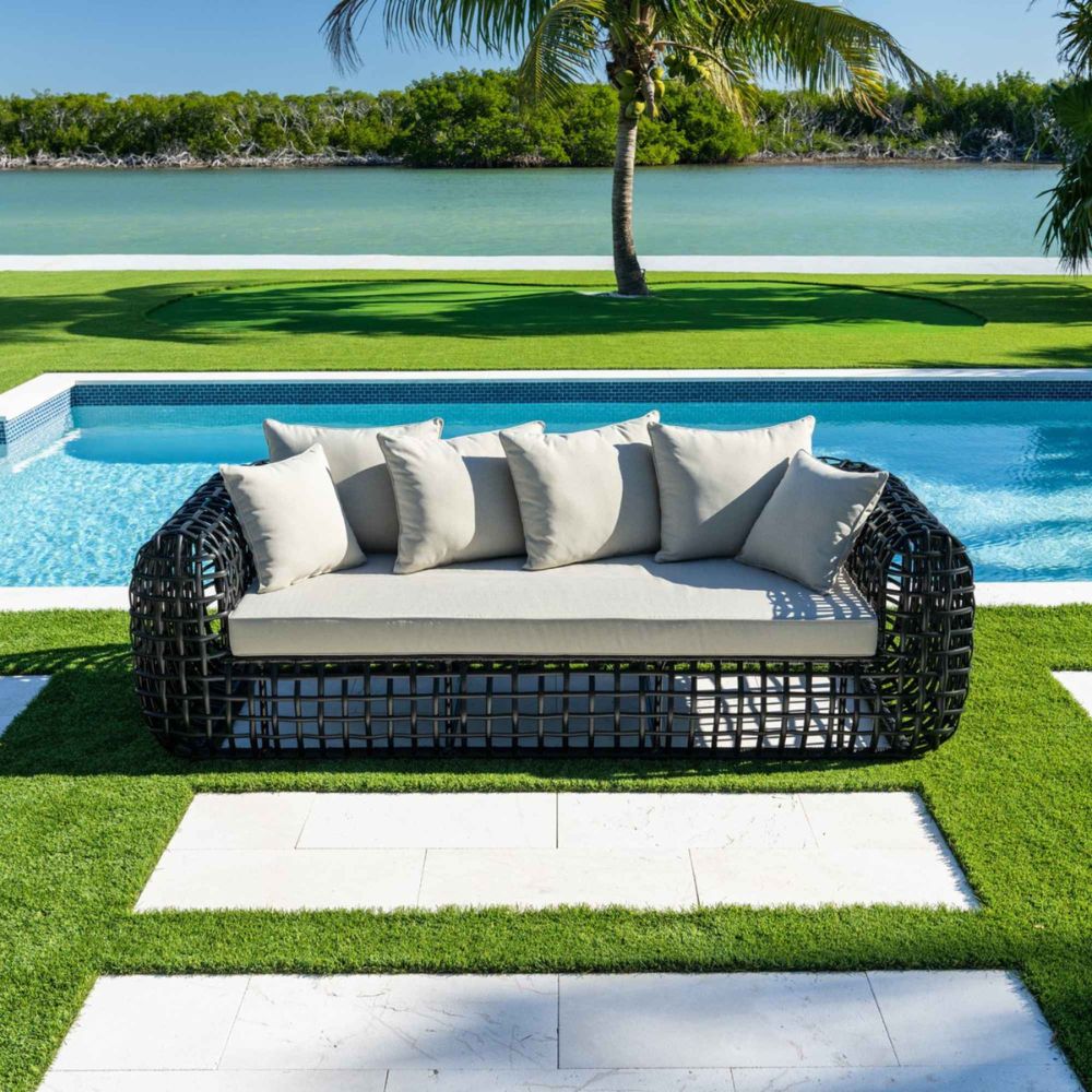 Outdoor sofa with cushions by a poolside with greenery