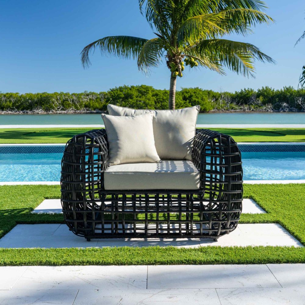 Black wicker chair with beige cushions by a poolside with palm trees in the background
