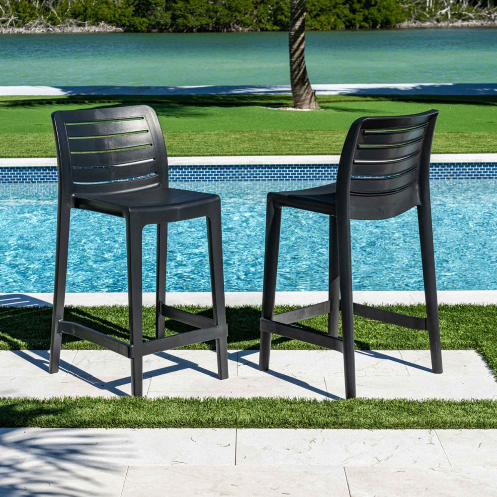 Two black outdoor bar stools by a pool with greenery in the background