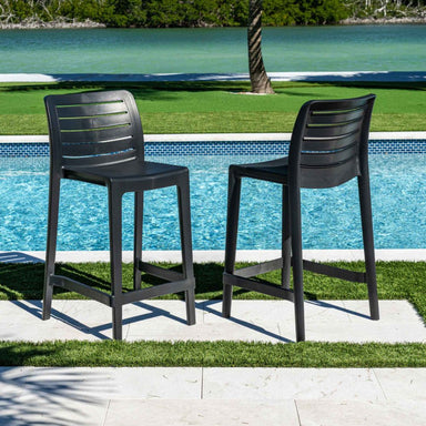 Two black outdoor bar stools by a pool with greenery in the background