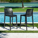 Two black outdoor bar stools by a pool with greenery in the background