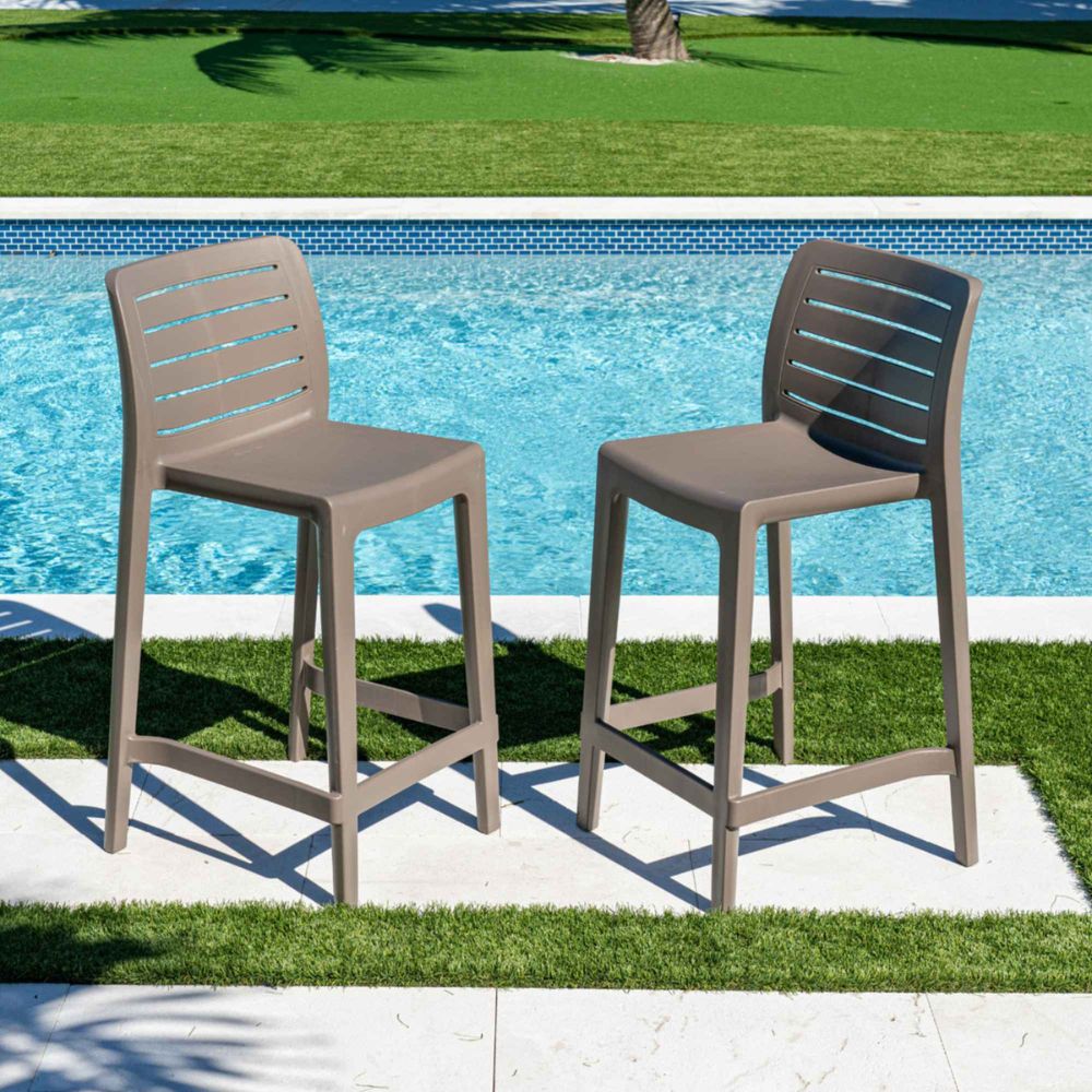 Two outdoor bar stools by a pool with grass and water in the background