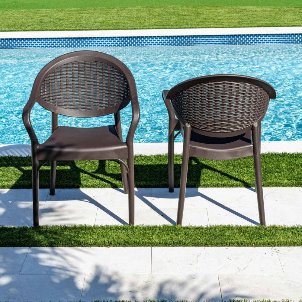 Two brown wicker chairs by a poolside on a sunny day.