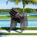 Stack of brown outdoor chairs by a pool with palm trees in the background