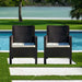 Two black wicker chairs with white cushions by a poolside.
