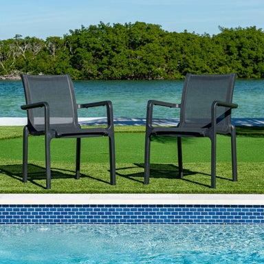 Two gray outdoor chairs on grass near a pool with trees in the background