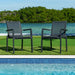Two gray outdoor chairs on grass near a pool with trees in the background