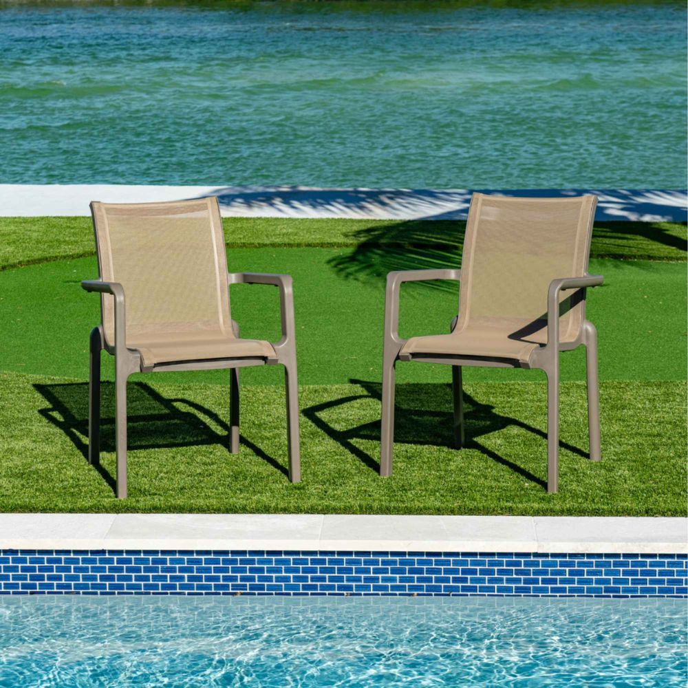 Two beige outdoor chairs on grass near a pool with water in the background